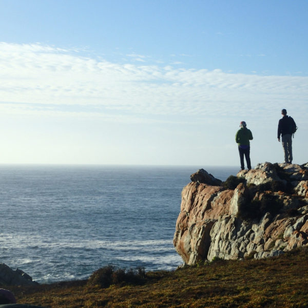 silhouette of two people standing on a rocky ridge overlooking the ocean