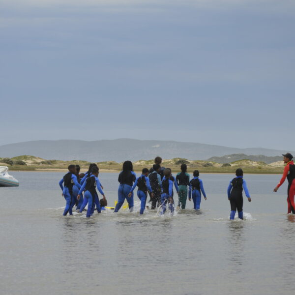 children in wetsuits with an instructor wading into a lagoon