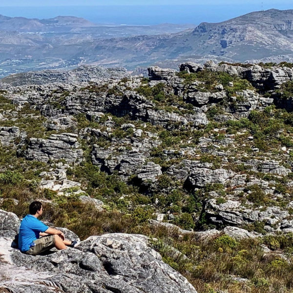 seated man on a hike amidst rocks looking over the mountain view of plettenberg bay