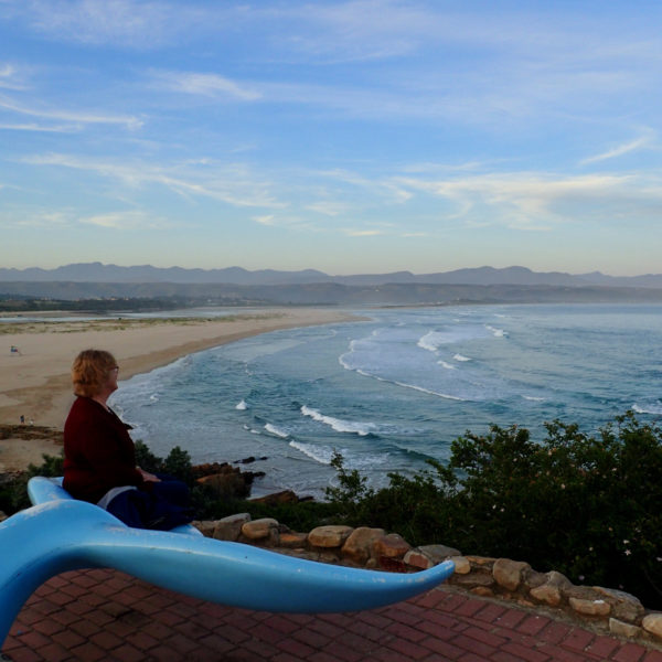 a woman sitting on a whale tail seat overlooking plettenberg bay